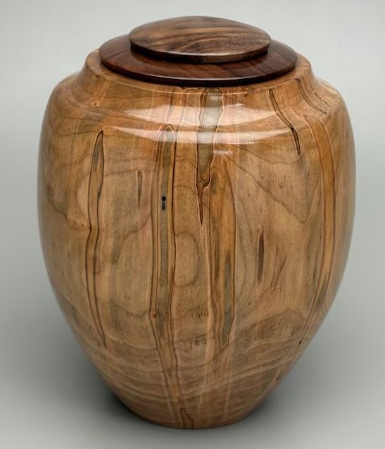 A glossy hand-turned urn of ambrosia maple, pale wood streaked with gray and brown lines, under a dark two-step wooden lid