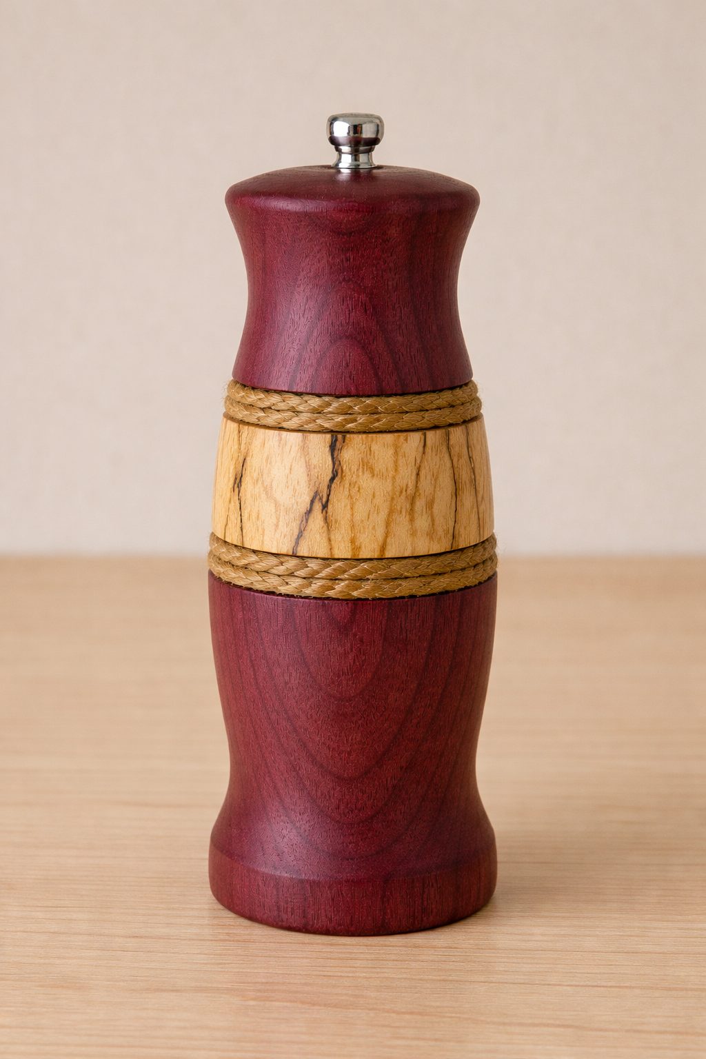 A tall hand-turned pepper mill in purpleheart with a band of spalted maple edged in braided cord