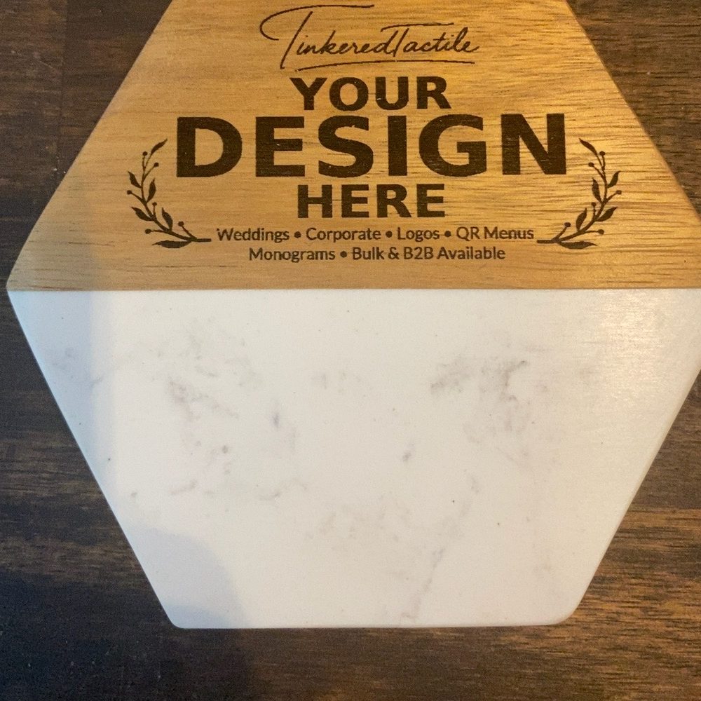 A hexagonal marble piece with a wood top, engraved 'Your design here' above a list: weddings, corporate, logos, QR menus, monograms, bulk and B2B